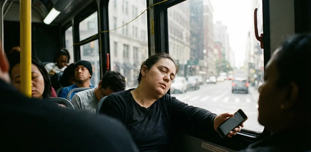 Людина дрімає вдень у громадському транспорті з телефоном у руці