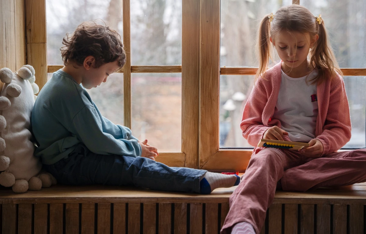 Children sitting separately by the window after an argument - relationship repair, tension after conflict, child's emotional recovery