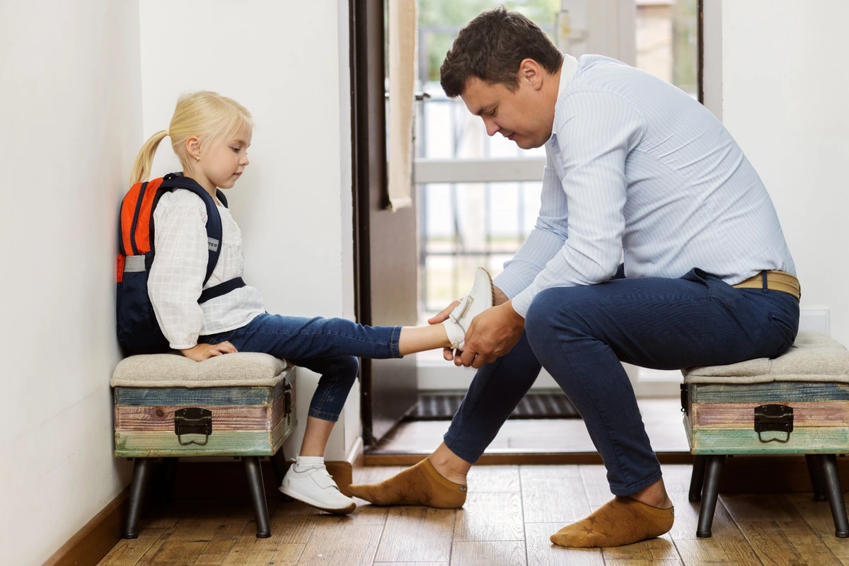 A parent helps a child put on shoes before leaving, without pressure or rushing