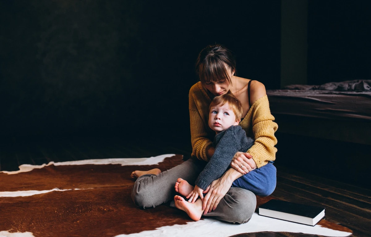 Мама сидить на підлозі й обіймає маленького сина в момент тривоги, напруги або потреби в близькості