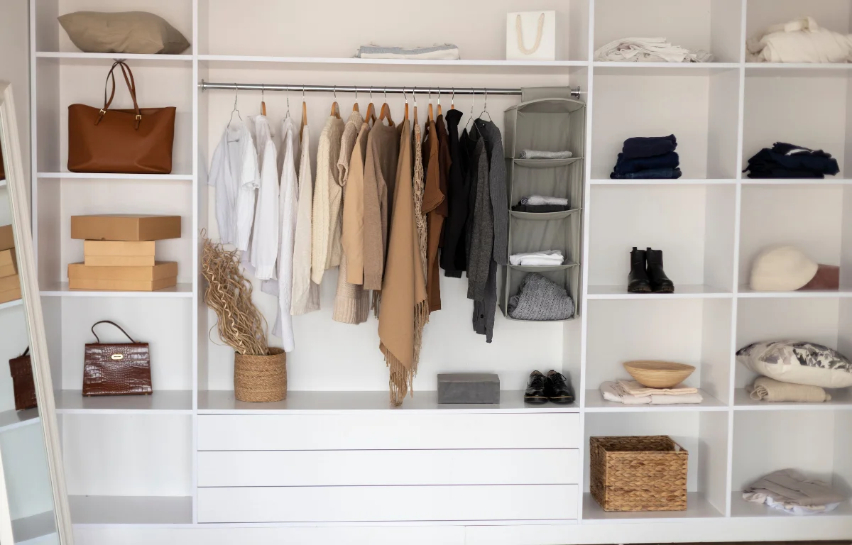 Open wardrobe with neutral clothing arranged on hangers and shelves in a calm interior
